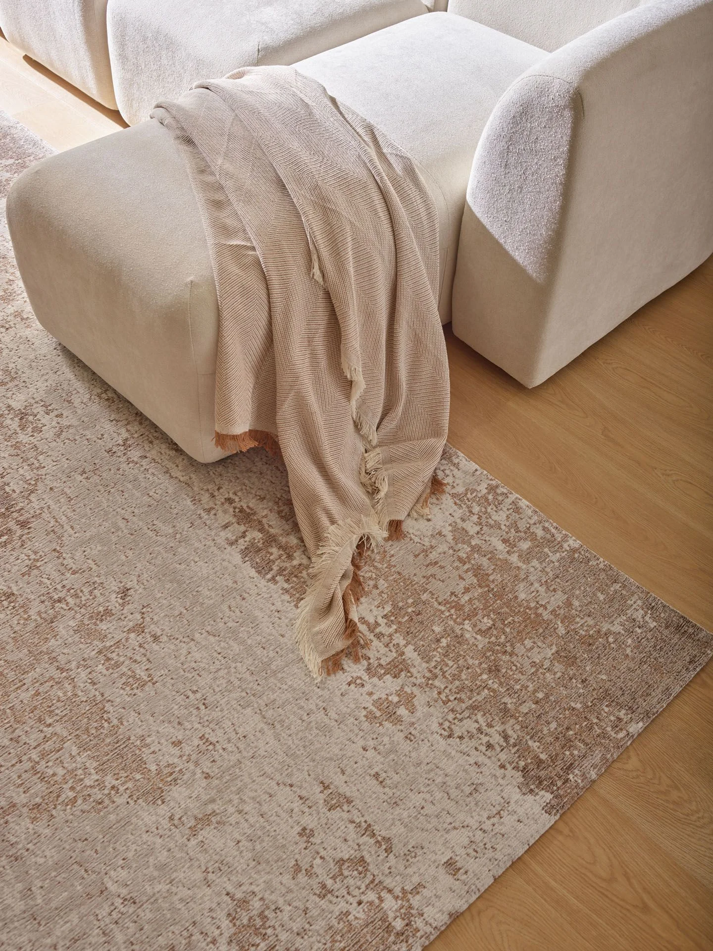 Modułowa jasna sofa z narzutą, ustawiona na beżowym dywanie